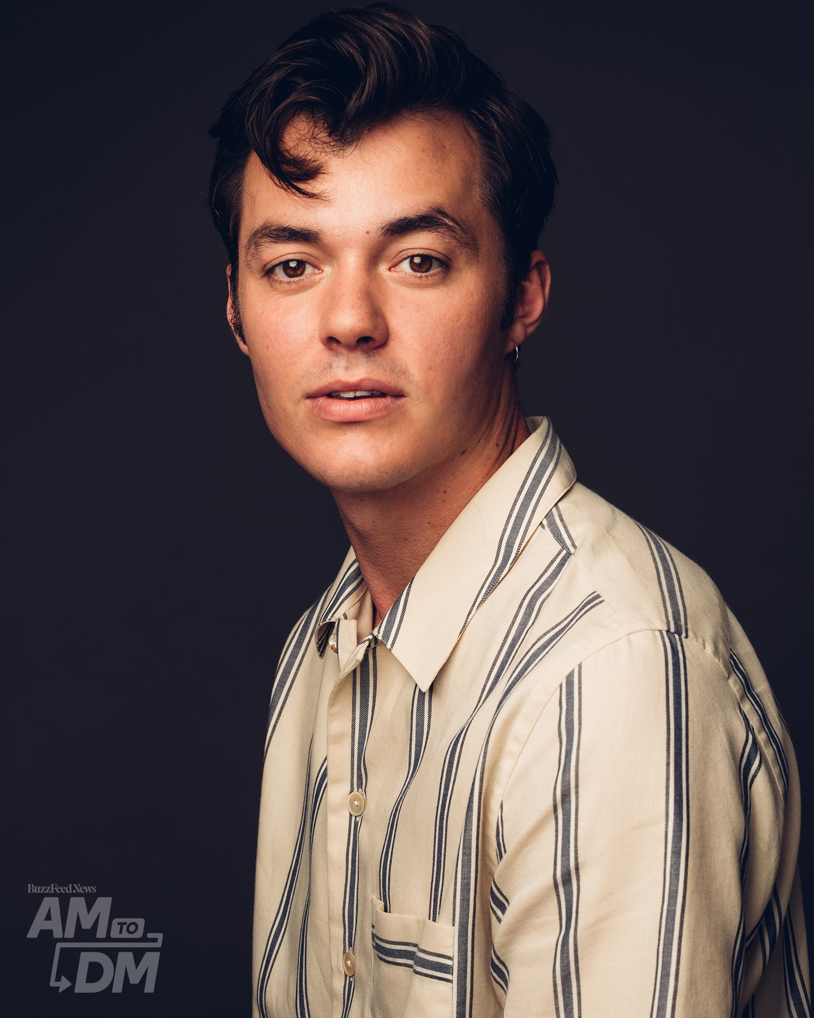 Portrait of Jack Bannon wearing a yellow and blue striped shirt in front of a dark gray background background. CREDIT: Taylor Miller / BuzzFeed News