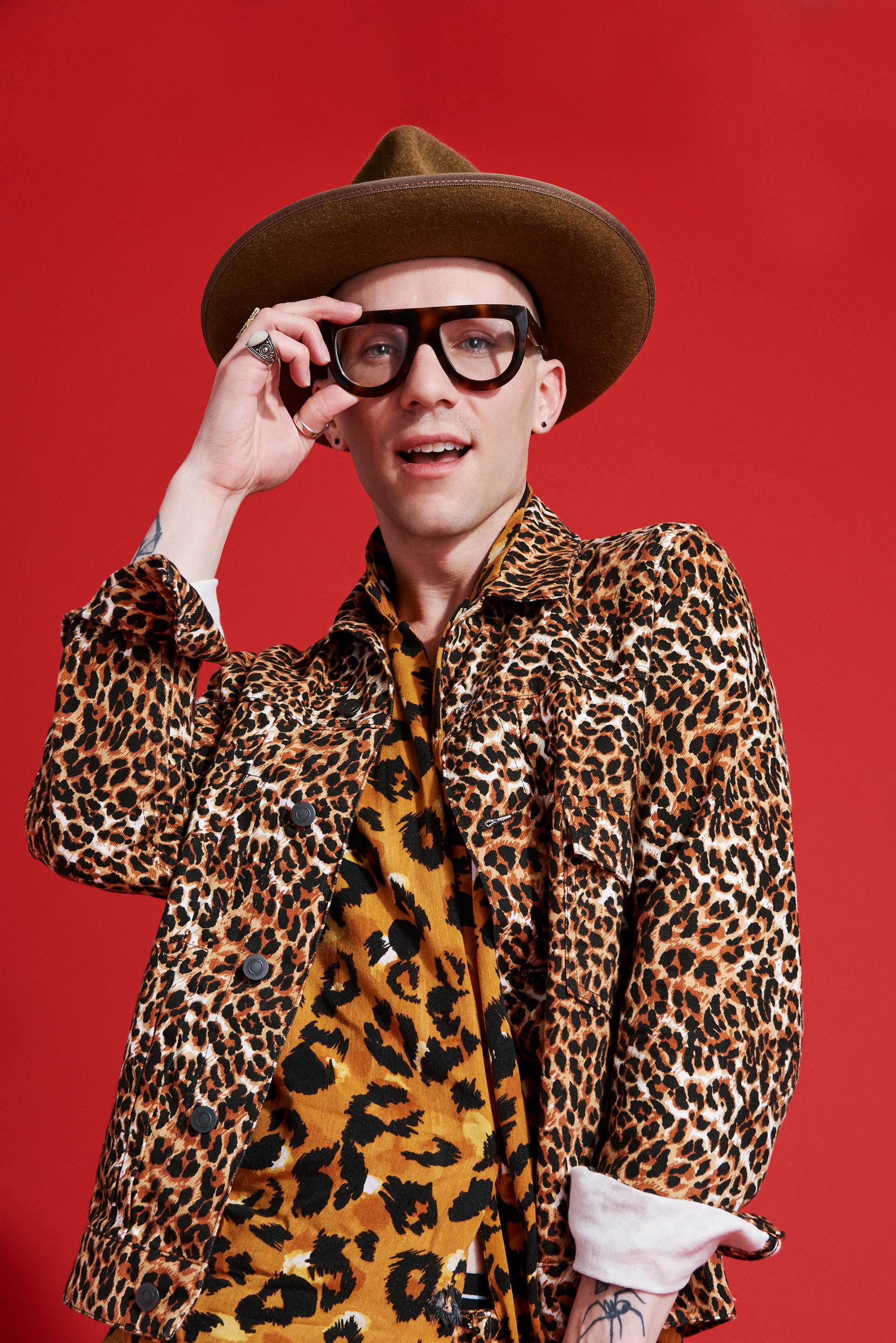 Portrait of Sasha Velour wearing a brown hat, a leopard print blazer over a leopard print shirt  in front of a red background. CREDIT: JJ Reddington / BuzzFeed News